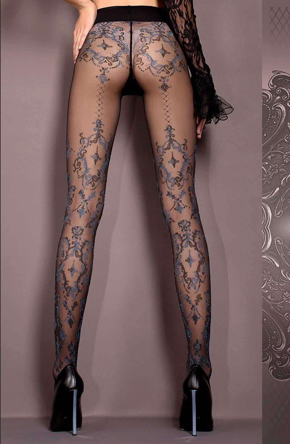 A person wearing Ballerina's Ballerina 412 Tights Nero (Black), black high heels, and a one-sleeved black lace top is standing against a neutral background with ornate detailing on the side. Part of the Hush Hush collection, these tights feature intricate designs running from the heels to the upper thighs.