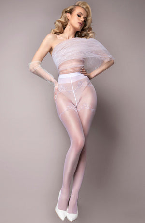 A woman with long blonde hair is wearing a sheer, sparkly off-shoulder top paired with Ballerina 580 White Tights from the Ballerina brand's Wedding Touch Collection. She completes her look with white high heels and poses gracefully, one leg slightly bent and one arm elegantly wrapped in the sheer fabric. The background is a plain, light gray.