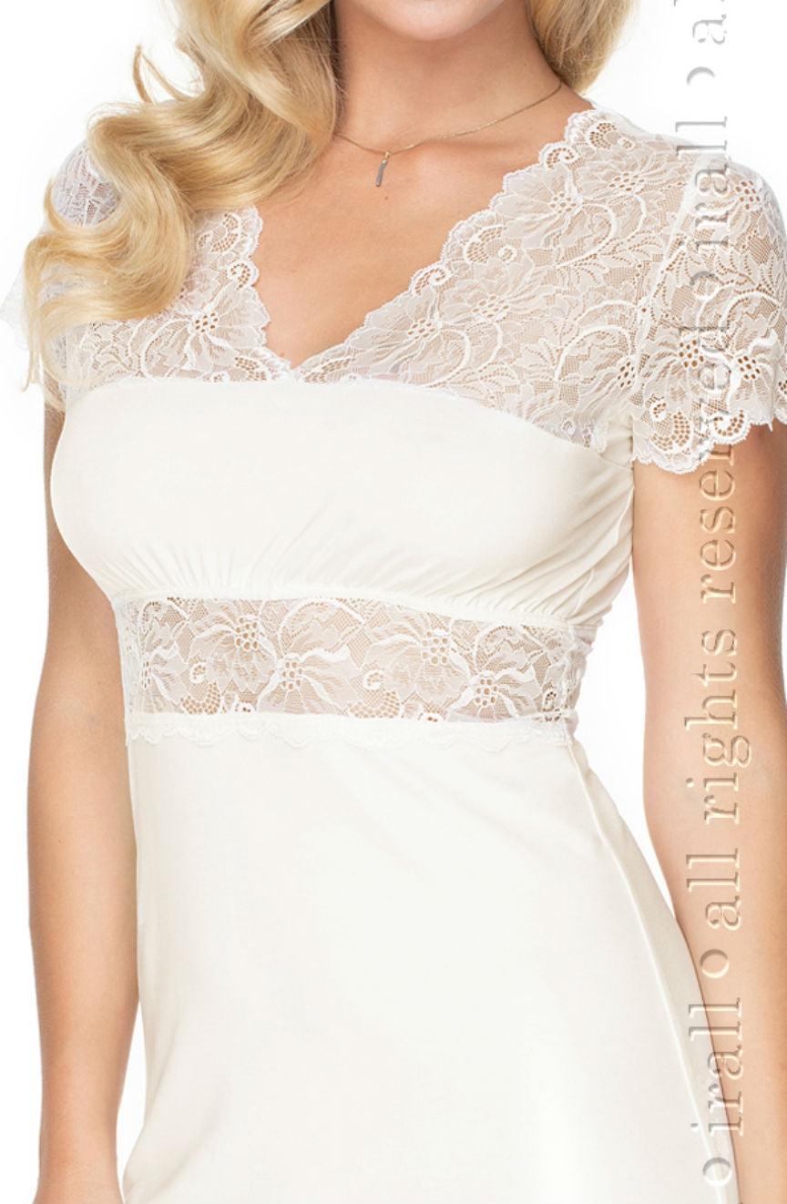 A woman wears the stunning Irall Cameron Nightdress in cream, showcasing intricate lace detailing around the neckline, sleeves, and midsection. This short-sleeved nightdress, available in sizes 2XL-5XL from the renowned brand Irall, is crafted from super soft fabric and perfectly complemented by her wavy blonde hair resting on her left shoulder.