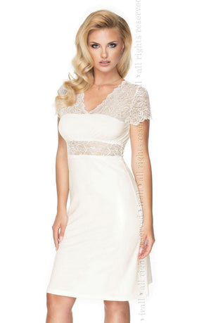 A woman with long blonde hair wears the elegant Irall Cameron Nightdress Cream by Irall, made of super soft fabric and featuring a V-neckline and short sleeves adorned with delicate lace details. She stands with her hands on the side of the dress against a plain white background.