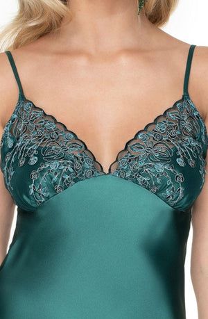 A woman wearing the Irall Emerald II Nightdress in dark green. This luxurious piece by Irall features delicate floral lace detailing along the neckline and straps, with intricate rose patterns in a slightly darker green and light silver thread. The thin straps and silky sheen of the fabric make it an exclusive addition to any wardrobe.