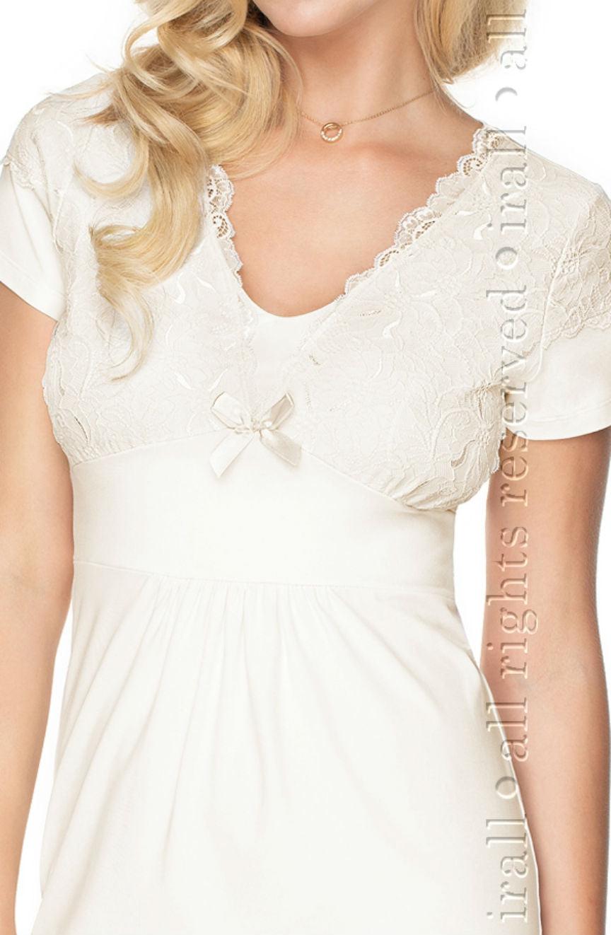 A person with long blond hair is seen wearing the elegant **Irall Gia Cream Nightdress** by **Irall**, made of delicate viscose and featuring a small bow at the center of the neckline. The cream-colored nightdress boasts short sleeves and intricate elastic lace detailing on the bodice. The person's face is not visible in the image.