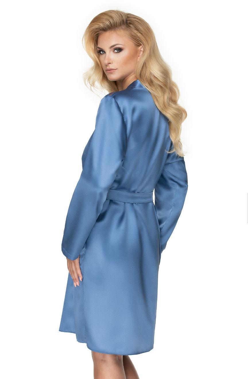 A person with long, wavy blonde hair is seen from the back, slightly turning to the side. They are wearing an Irall Sapphire Dressing Gown Azure by Irall, a high-quality satin robe in light blue that ties at the waist. The background is plain white.