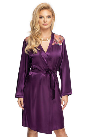 A woman with long blonde hair stands wearing the Irall Shelby Dressing Gown in purple, crafted from satin and featuring floral embroidery on the shoulders. The robe, an elegant piece by the brand Irall, is cinched at the waist with a matching satin belt. She accessorizes with a gold chain necklace and poses against a plain white background.