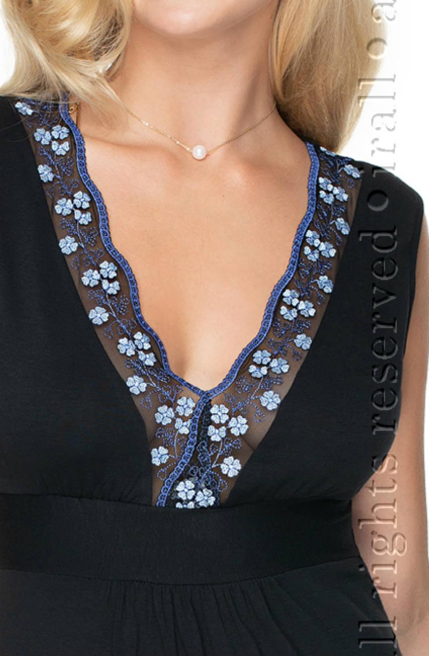 Close-up of a person wearing the Irall Titania Nightdress Black by Irall, which features a deep V-neckline adorned with sheer fabric showcasing blue floral embroidery. The individual is also wearing a delicate pearl necklace.