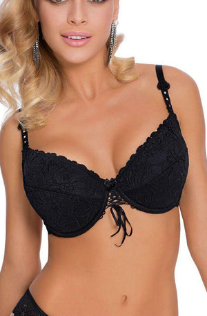 A woman is wearing a Roza Damaris Black Bra by Roza, paired with matching black lace underwear. With her blonde, wavy hair cascading down, she is adorned with long, dangling earrings. The bra features intricate decorative lace and a ribbon detail in the center. She strikes a pose against a plain background.