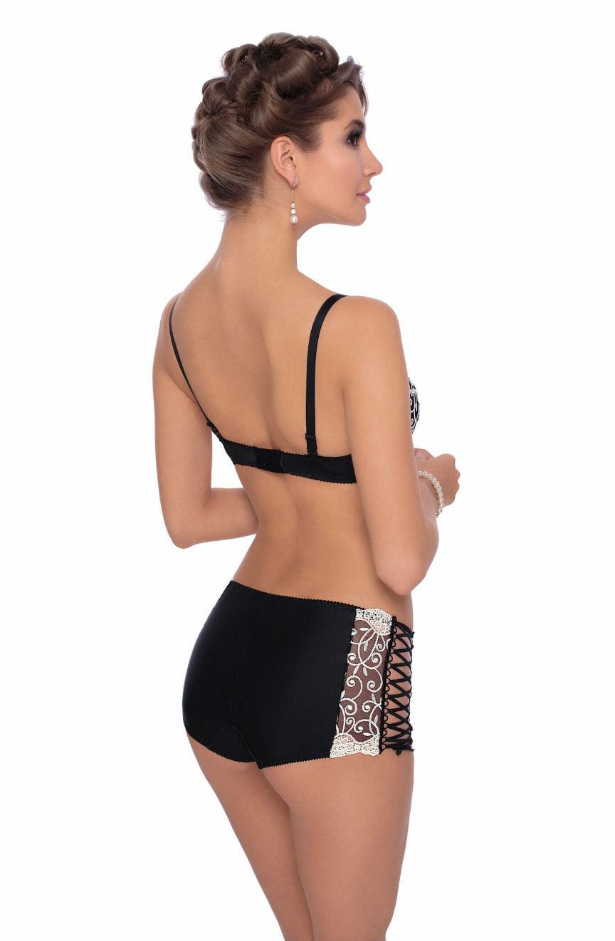 A woman with an elegant updo hairstyle is wearing lingerie, featuring a matching push-up bra and the Roza Ginewra Short by Roza. The black high-waisted shorts highlight intricate lace designs and crisscross ribbon detailing on the back. She faces sideways with her hands held softly in front of her.