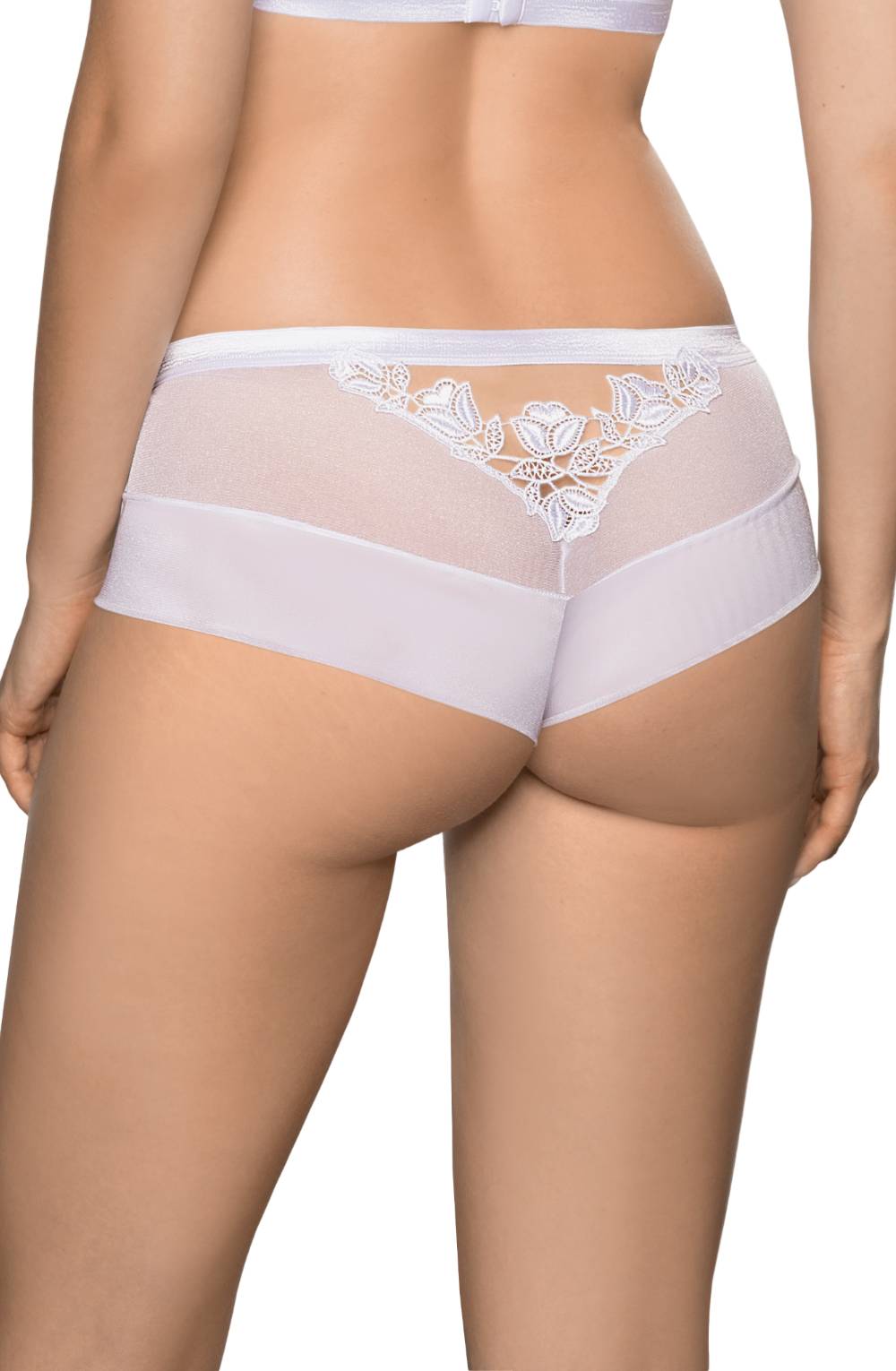 A woman is seen from the back wearing a Roza Lisbet White Brief in a white lace lingerie set from Roza. The lace details with floral appliqué form intricate patterns on the underwear, combining mesh and luxurious stretch fabric. Her figure is mostly visible, showcasing the lingerie’s fit and style.