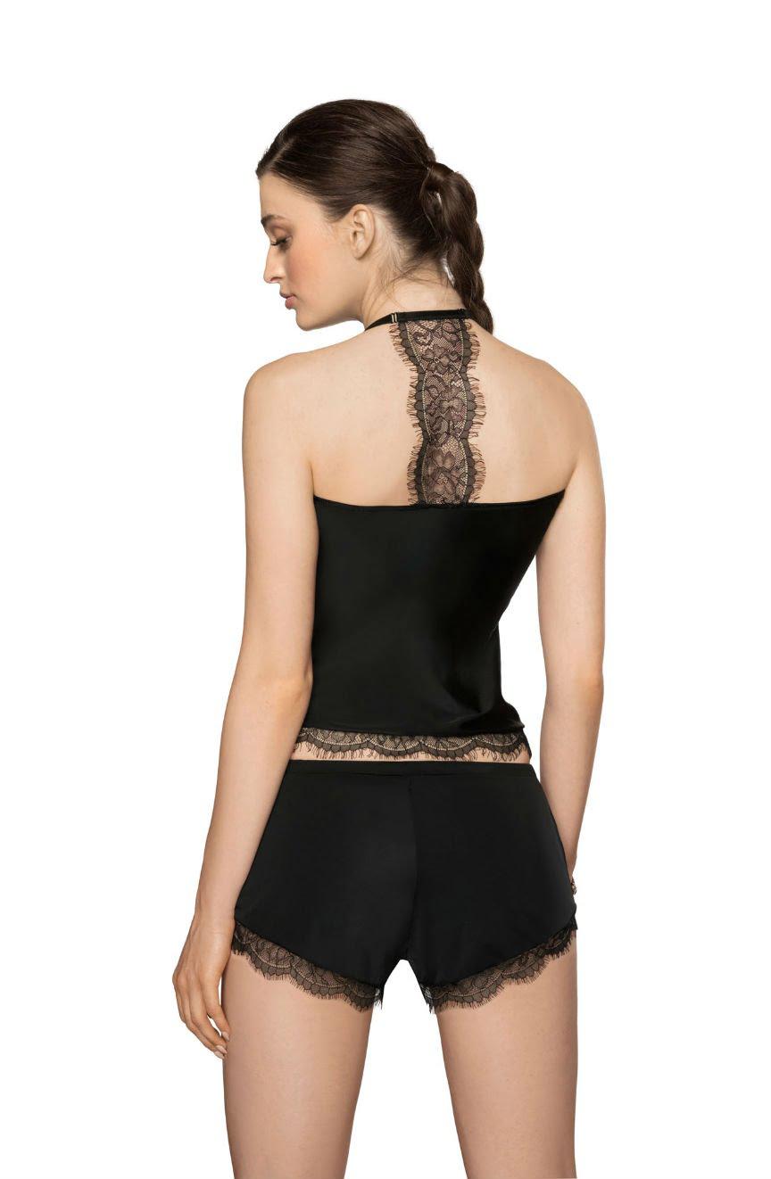 A woman stands with her back to the camera, modeling the Roza Sija Black Nightshirt from Roza. The nightshirt features a halter-neck design and intricate lace detailing, paired with matching black shorts also adorned with eyelash lace. Her long dark hair is styled in a side braid. The soft stretch fabric promises comfort against a plain white background.