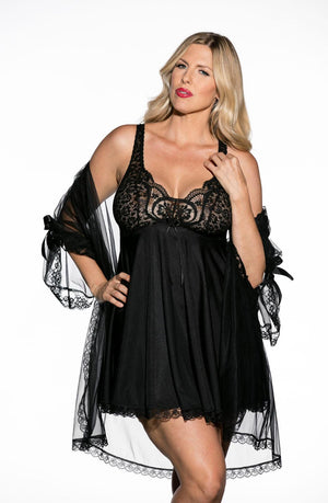 A woman with blonde hair poses confidently, dressed in the elegant Shirley Of Hollywood X3595 Black 3 Piece Babydoll lingerie set by Shirley of Hollywood. The outfit features stretch lace cups, intricate patterns on the sheer top, and matching mesh fabric. She completes the look with a sheer lace robe adorned with ribbon ties on the sleeves, epitomizing elegance and allure.