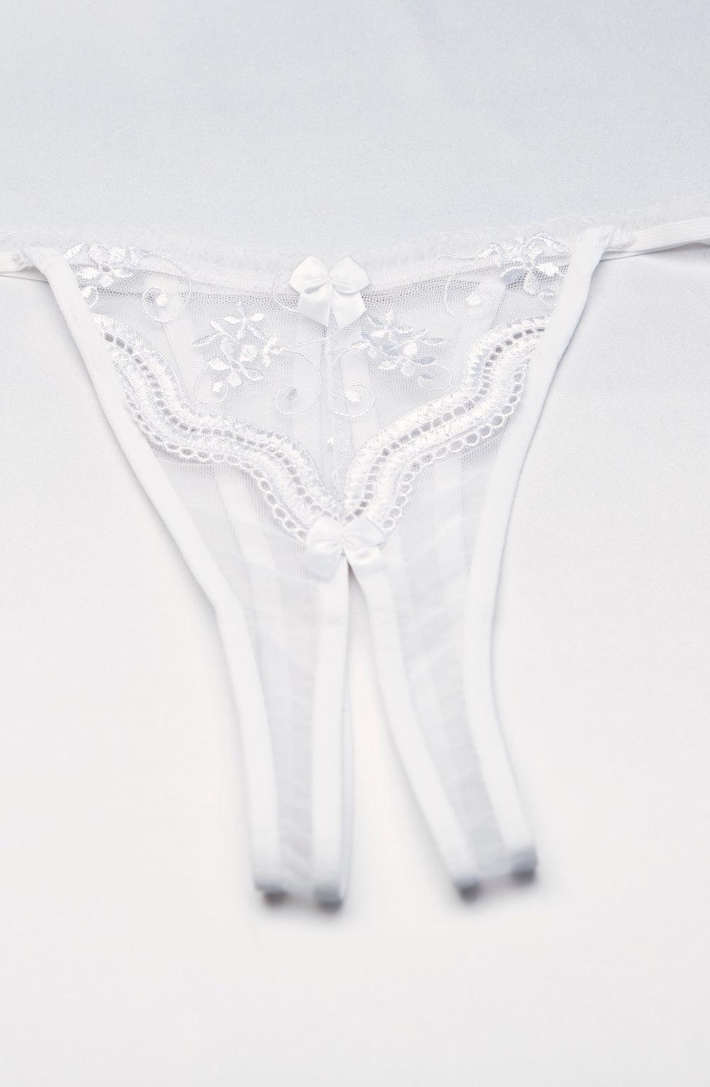 The Shirley Of Hollywood Crotchless Thong in white is displayed, featuring delicate floral scalloped embroidery and a charming small bow in the center. The sheer and lightweight fabric lends an elegant and feminine touch to the design. Plus sizes are available for a perfect fit.