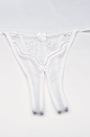 The Shirley Of Hollywood Crotchless Thong in white is displayed, featuring delicate floral scalloped embroidery and a charming small bow in the center. The sheer and lightweight fabric lends an elegant and feminine touch to the design. Plus sizes are available for a perfect fit.