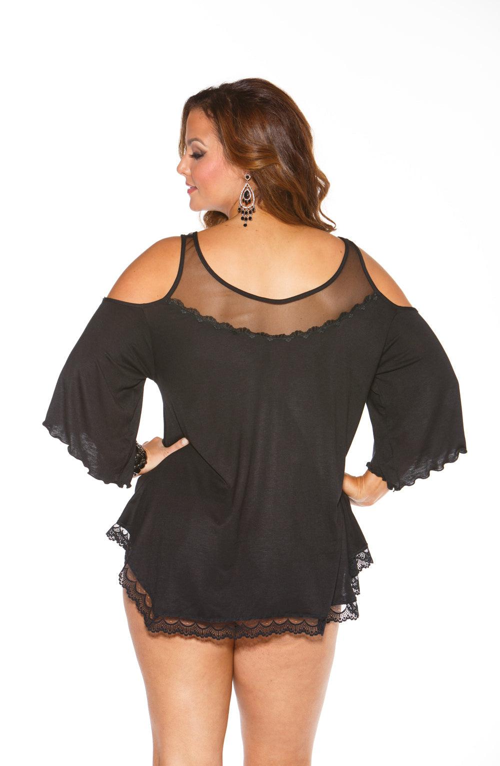 A woman with long brown hair is posing in the Shirley Of Hollywood X3257 Sleepshirt Black, which features lace trim on the sleeves and hem and is crafted from soft Rayon Jersey Knit. She is facing away from the camera and wearing statement earrings. The background is plain white.