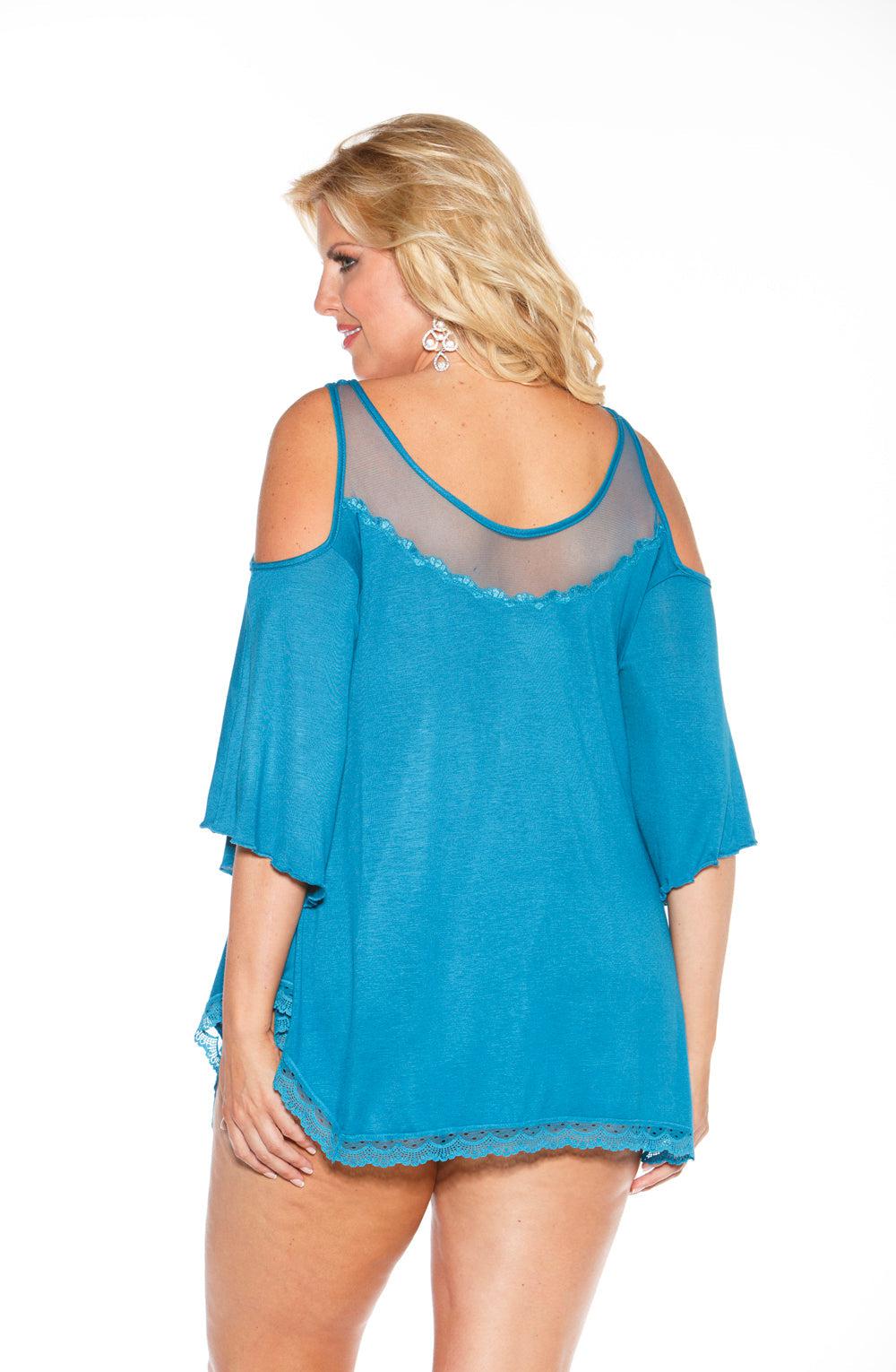 A woman with blonde hair is modeling the Shirley of Hollywood X3257 Sleepshirt in Sapphire. The outfit features an off-the-shoulder design with sheer net lace and detailing on the back. She is turned slightly to the side, showcasing both the back and side of the sleepshirt, which has loose sleeves ending above the elbow.