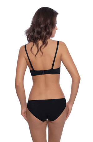 A woman with wavy brown hair is shown from behind, wearing the Vangelise Brief Black by Roza, a black bra and matching underwear adorned with floral embroidery. She stands facing away from the camera, highlighting the intricate back design of her lingerie against an uncluttered white background.