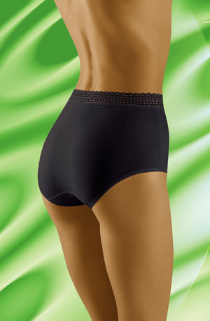 The image displays a person wearing the Wolbar Eco-Go Black Brief from Wolbar, characterized by its high-quality cotton construction and delicate lace trim along the waistband. The individual is slightly turned to the side, highlighting the fit of the underwear against a background featuring a blended pattern of green and white swirls.